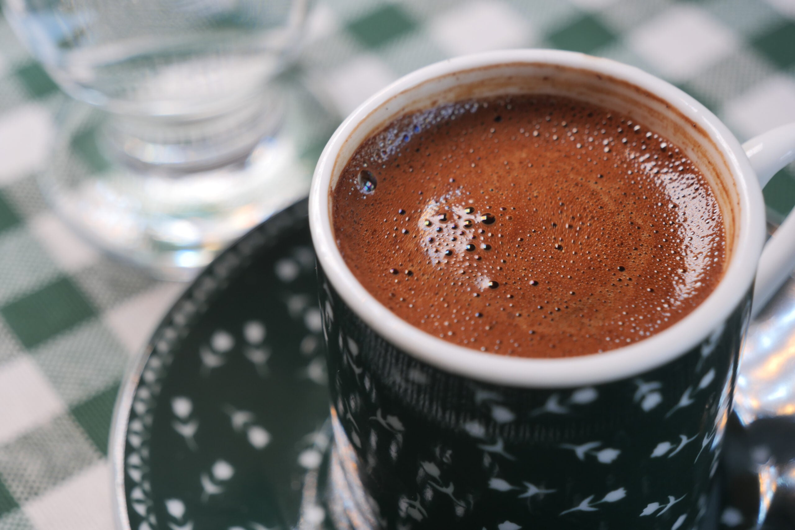Duke shijuar kafe turke në një ambient komod kafeneje me mbulesë tavoline me kuadrata