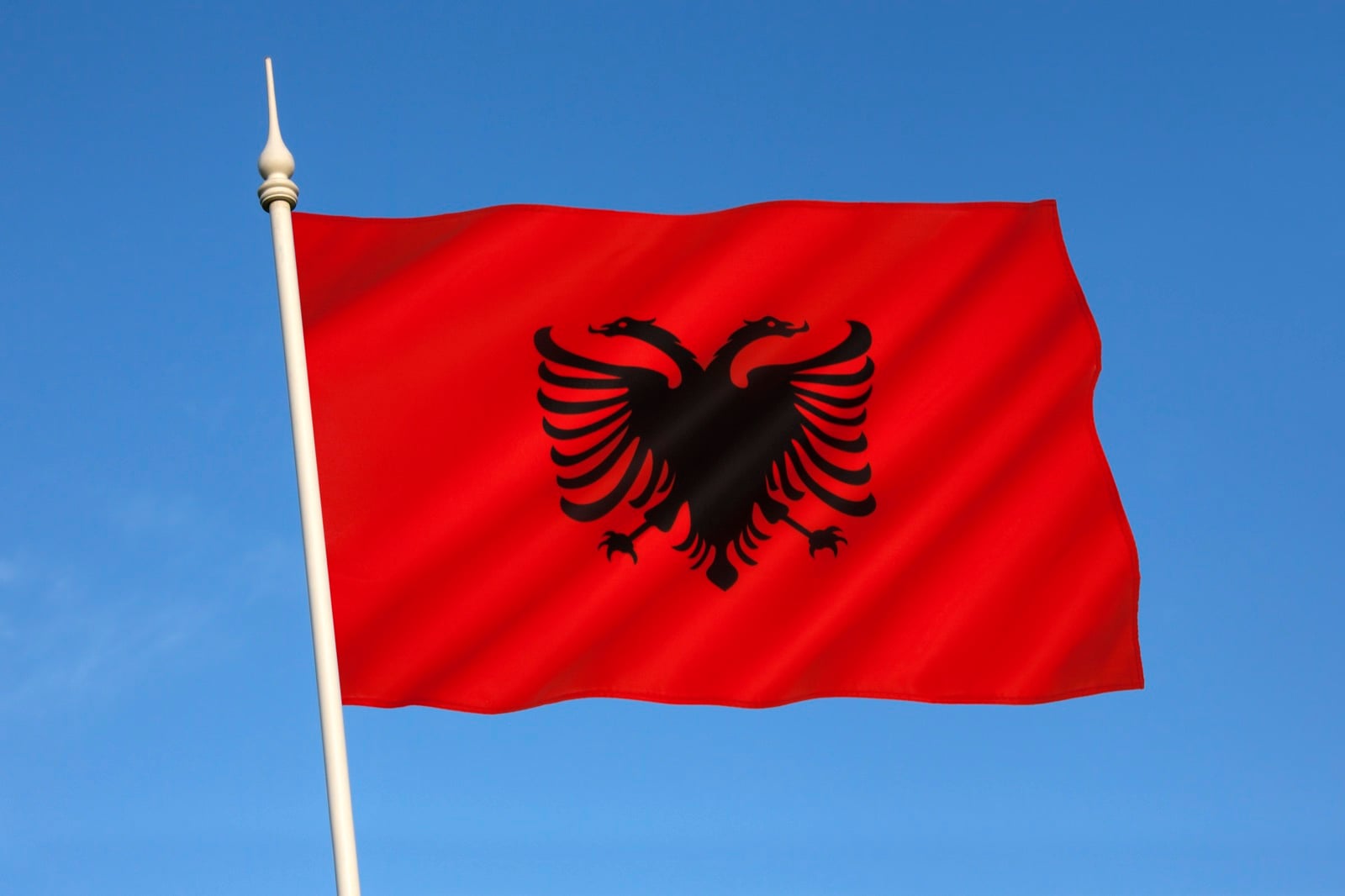 The Albanian flag, red with a black double-headed eagle, waving against a blue sky