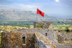 Albanian flag waving above stone castle walls