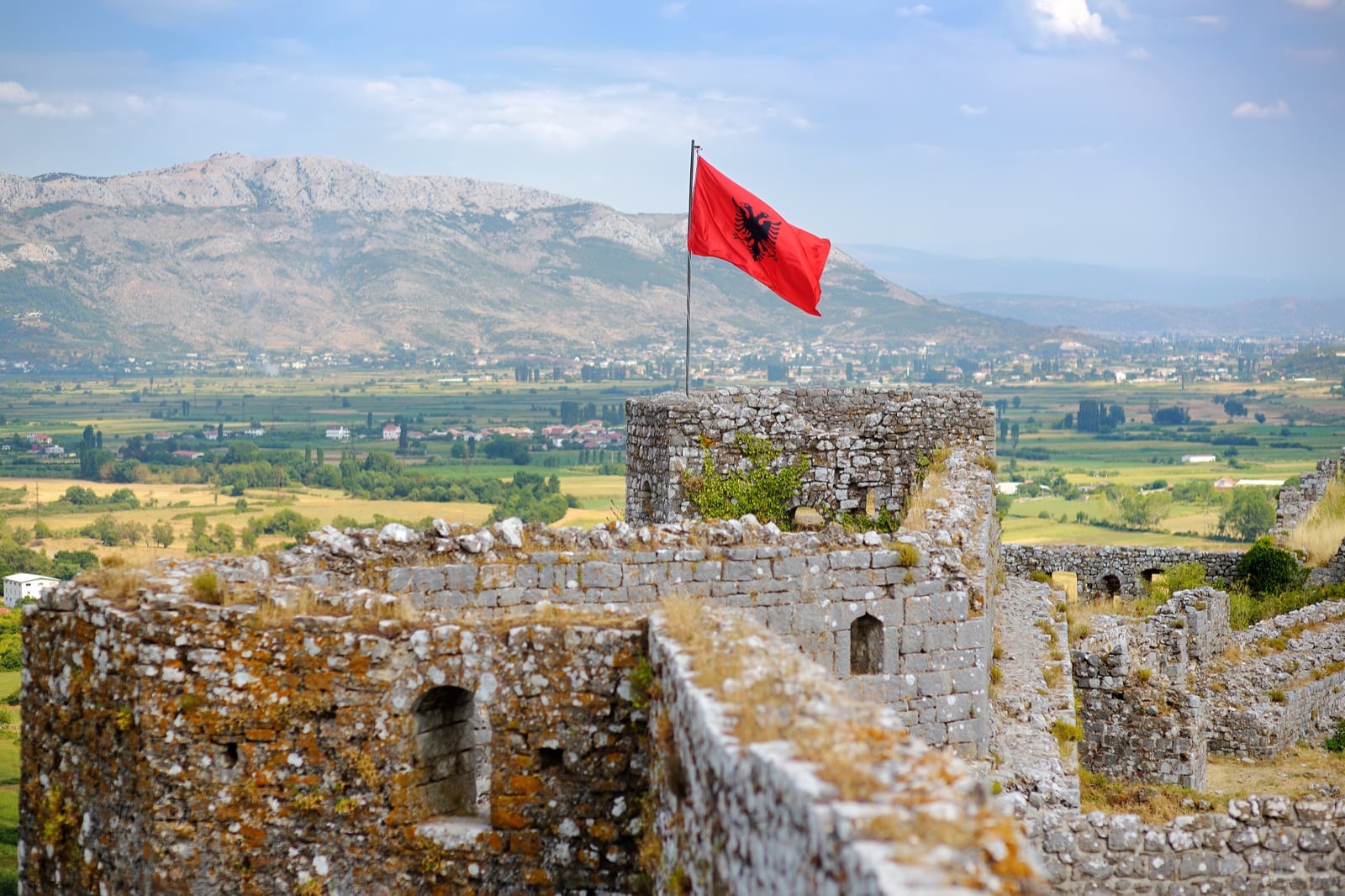Albanian flag waving above stone castle walls