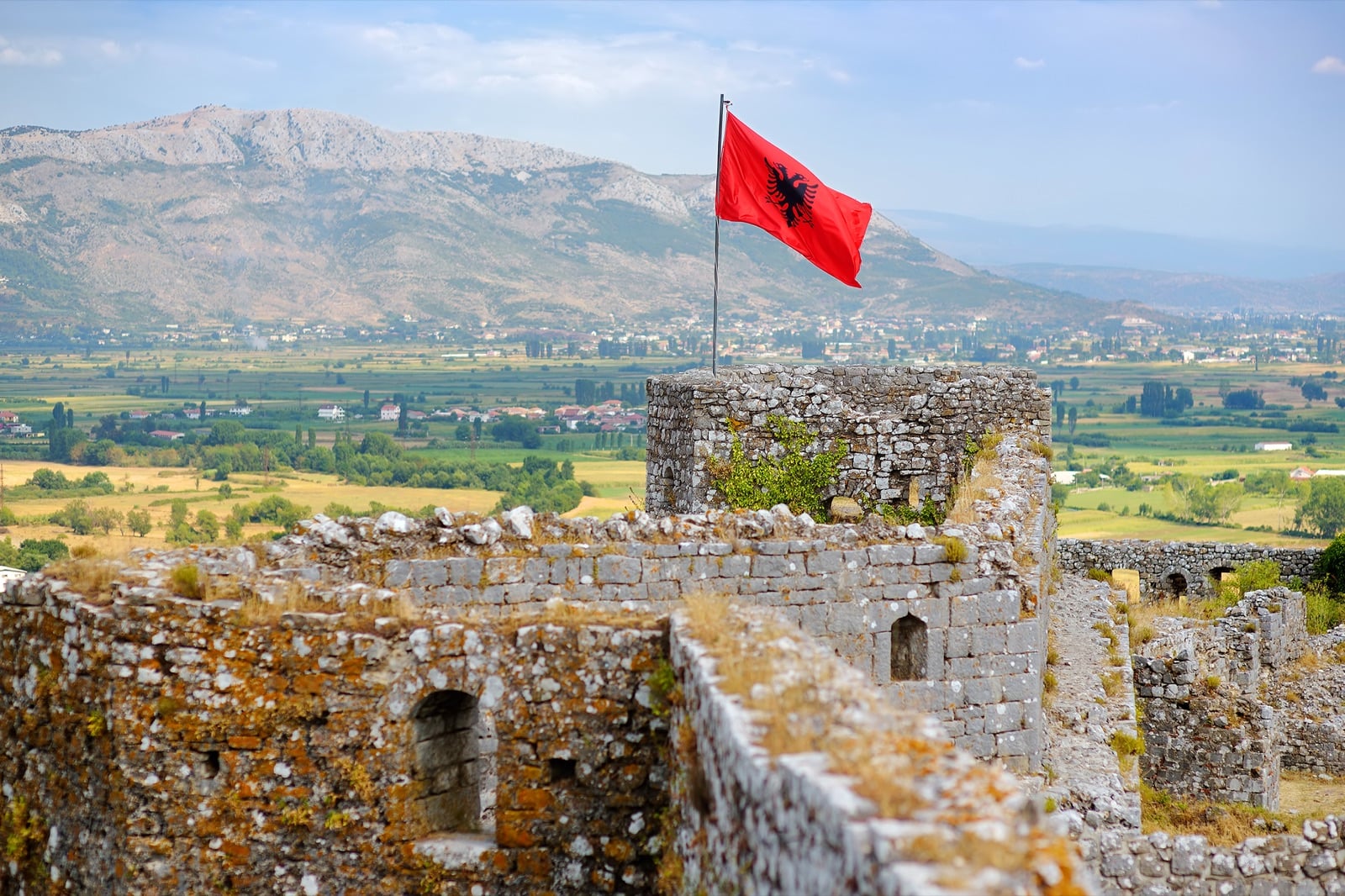 Albanian flag flying above ancient fortress ruins