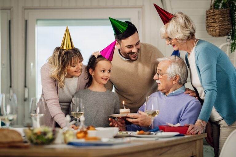 A family celebrating a grandfather's birthday at home with cake and party hats