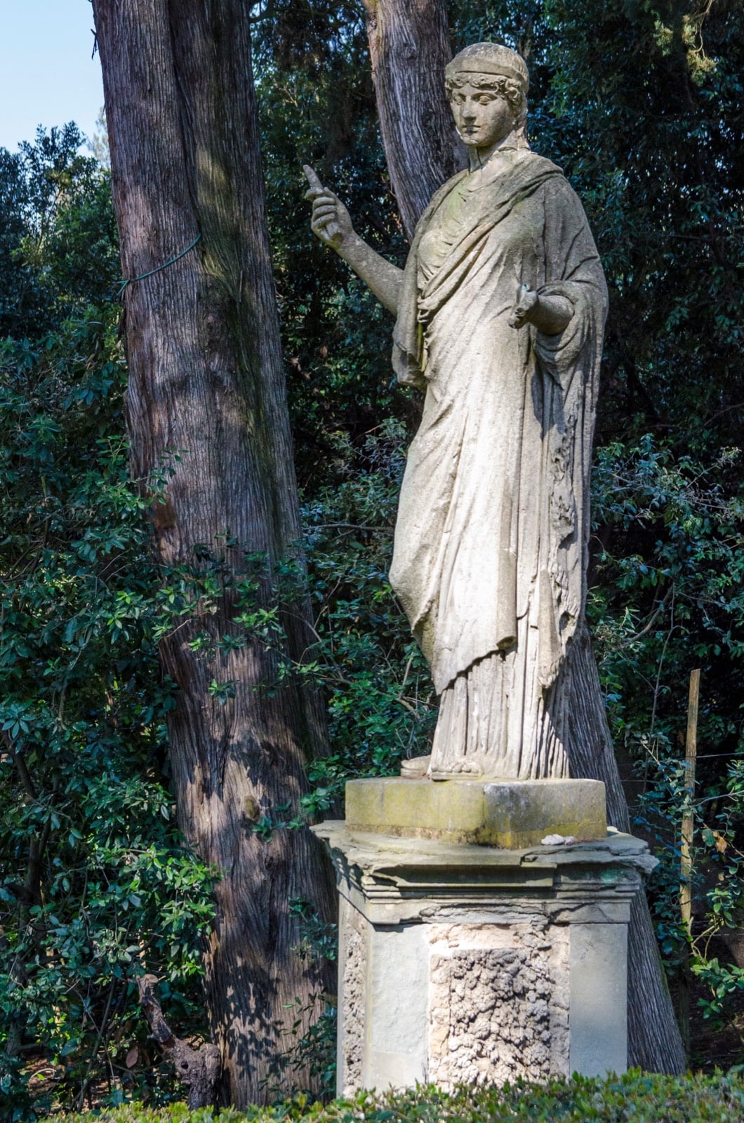 Weathered stone statue of a robed figure standing among trees