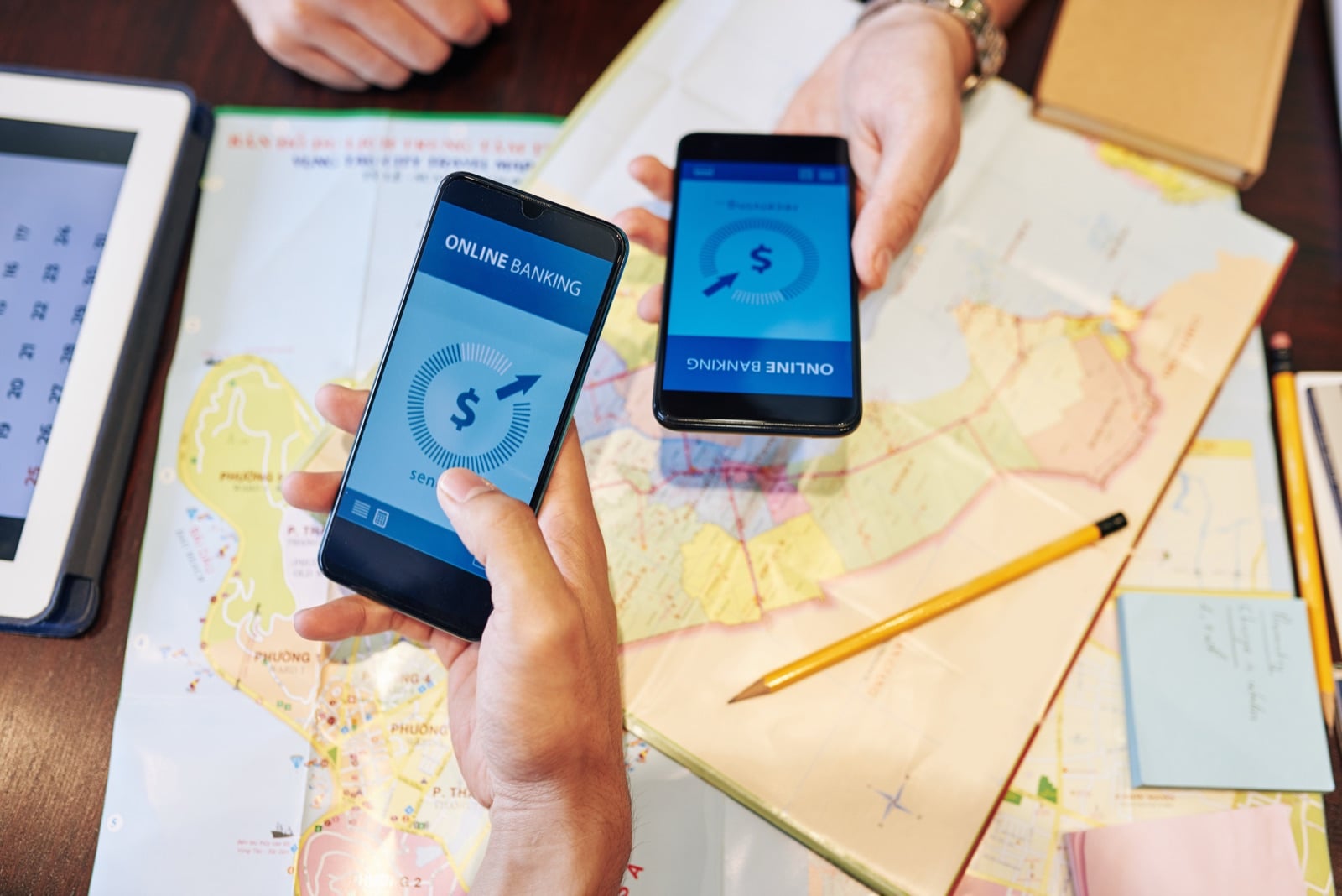 Two people holding smartphones with a banking app over a map, illustrating an international money transfer