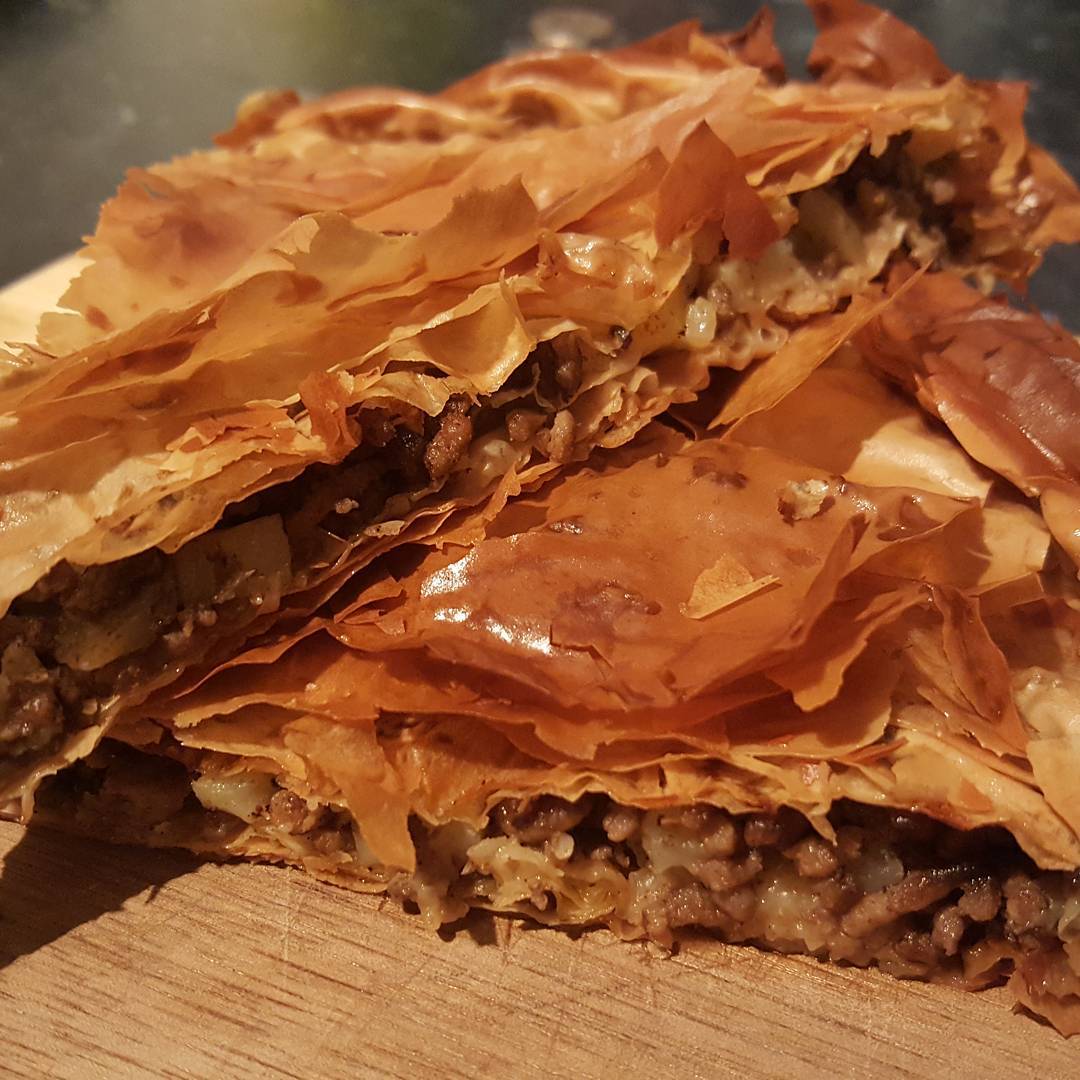 Byrek me mish: layered filo pie with a minced meat filling, cut open on a wooden board